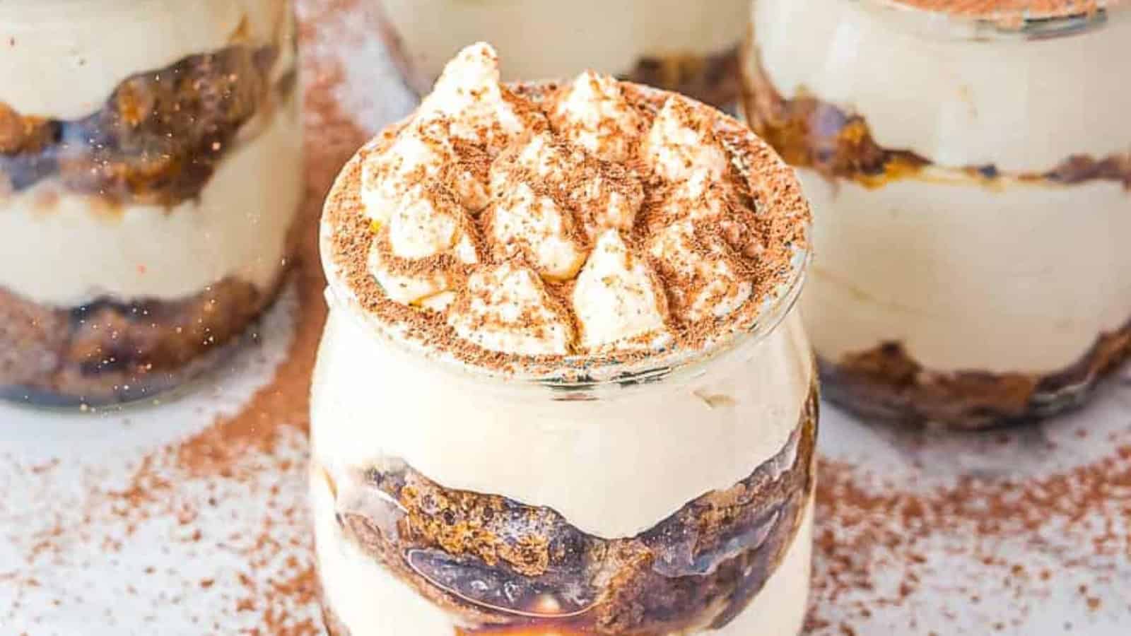 Two glass jars of tiramisu topped with cocoa and chocolate shavings, next to pieces of dark chocolate.