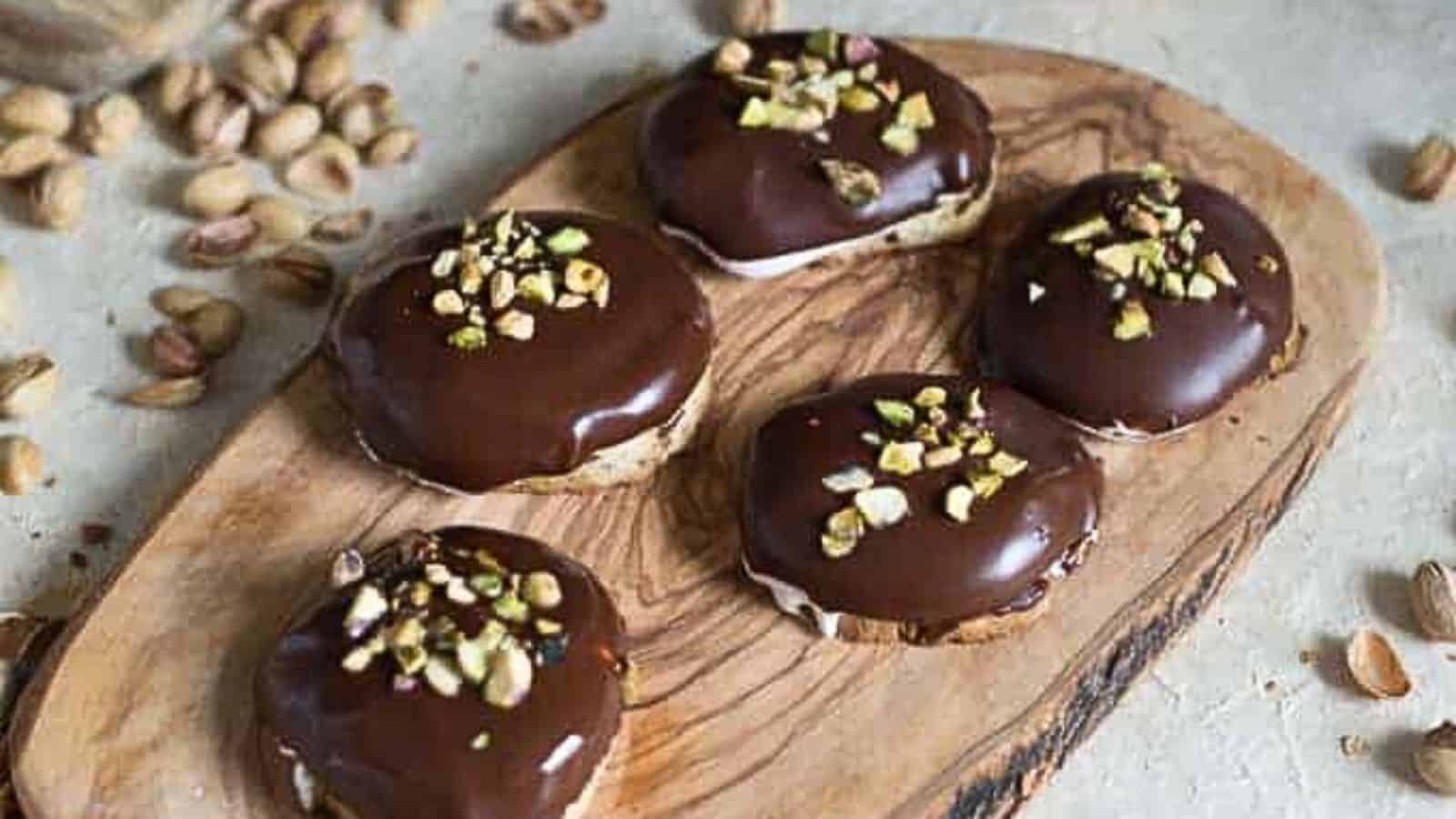 Chocolate covered pistachio cookies on a wooden cutting board.