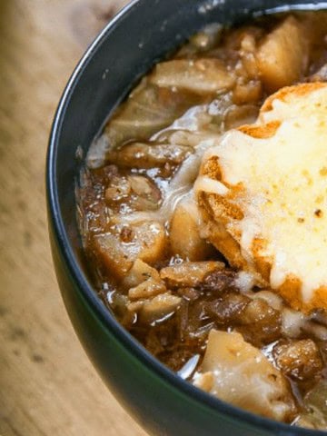 A bowl of French onion soup with melted cheese on bread, garnished with parsley, next to sliced baguette.