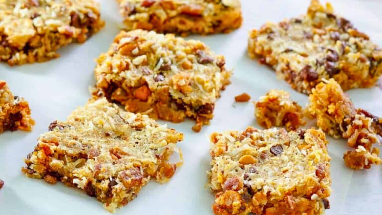 Seven homemade granola bars with oats, nuts, and chocolate chips on a white surface.