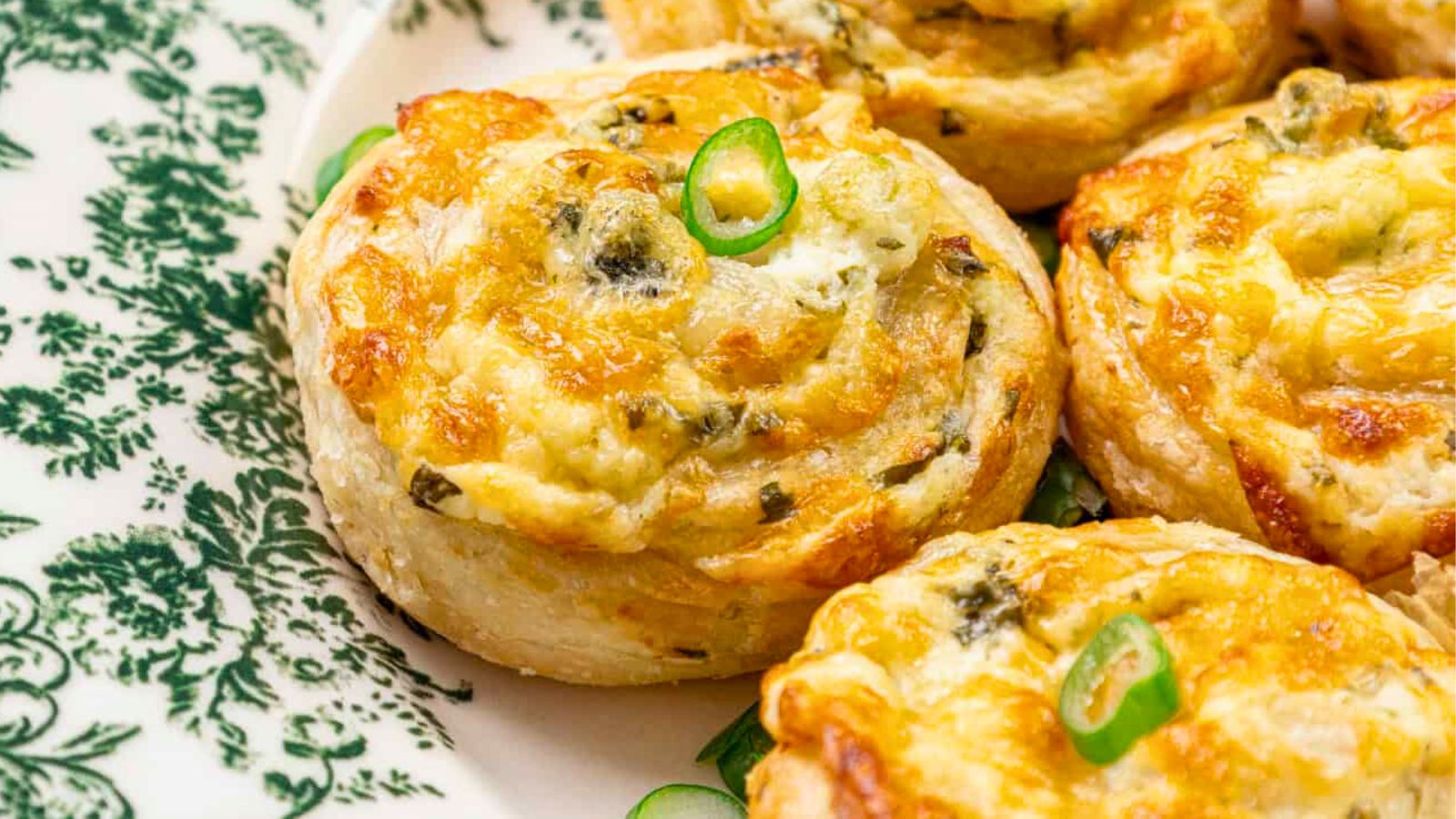Baked pastry rolls with cheese and herbs on a decorative green and white plate.