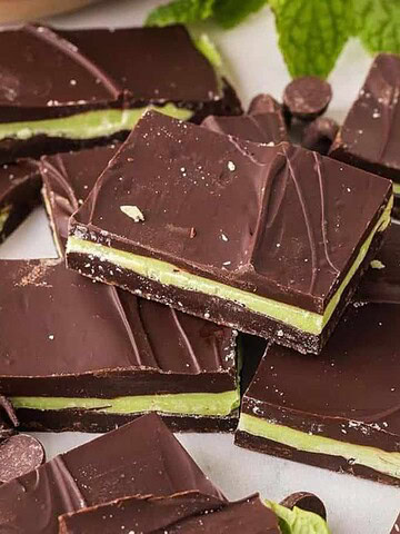 Squares of chocolate mint bars with a green mint layer, surrounded by chocolate chips and fresh mint leaves.