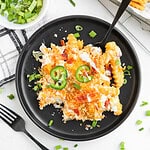 A serving of cheesy casserole topped with jalapeño slices and green onions on a black plate with a fork, inspired by the flavors of a jalapeno popper loaded cheese fries recipe.