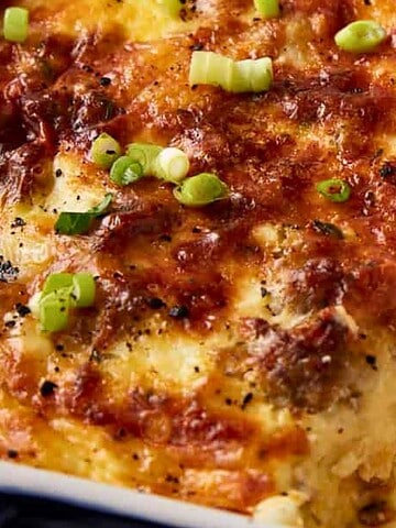 A casserole dish of cheesy baked egg and sausage breakfast casserole, one of the most comforting breakfast casseroles, topped with chopped green onions.