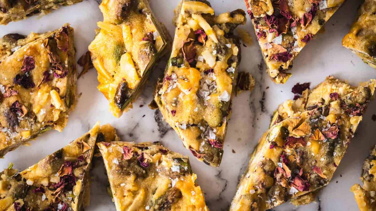 Close-up of nut and fruit bars topped with dried flower petals and sea salt on a marble surface.