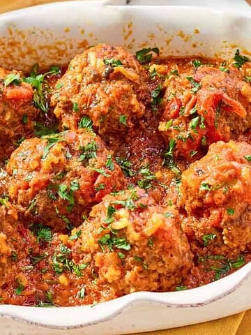 Meatballs in tomato sauce, garnished with chopped parsley, served in a white baking dish.