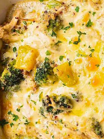 Cheesy chicken, broccoli, and yellow squash casserole topped with melted cheese and chopped parsley in a white dish.