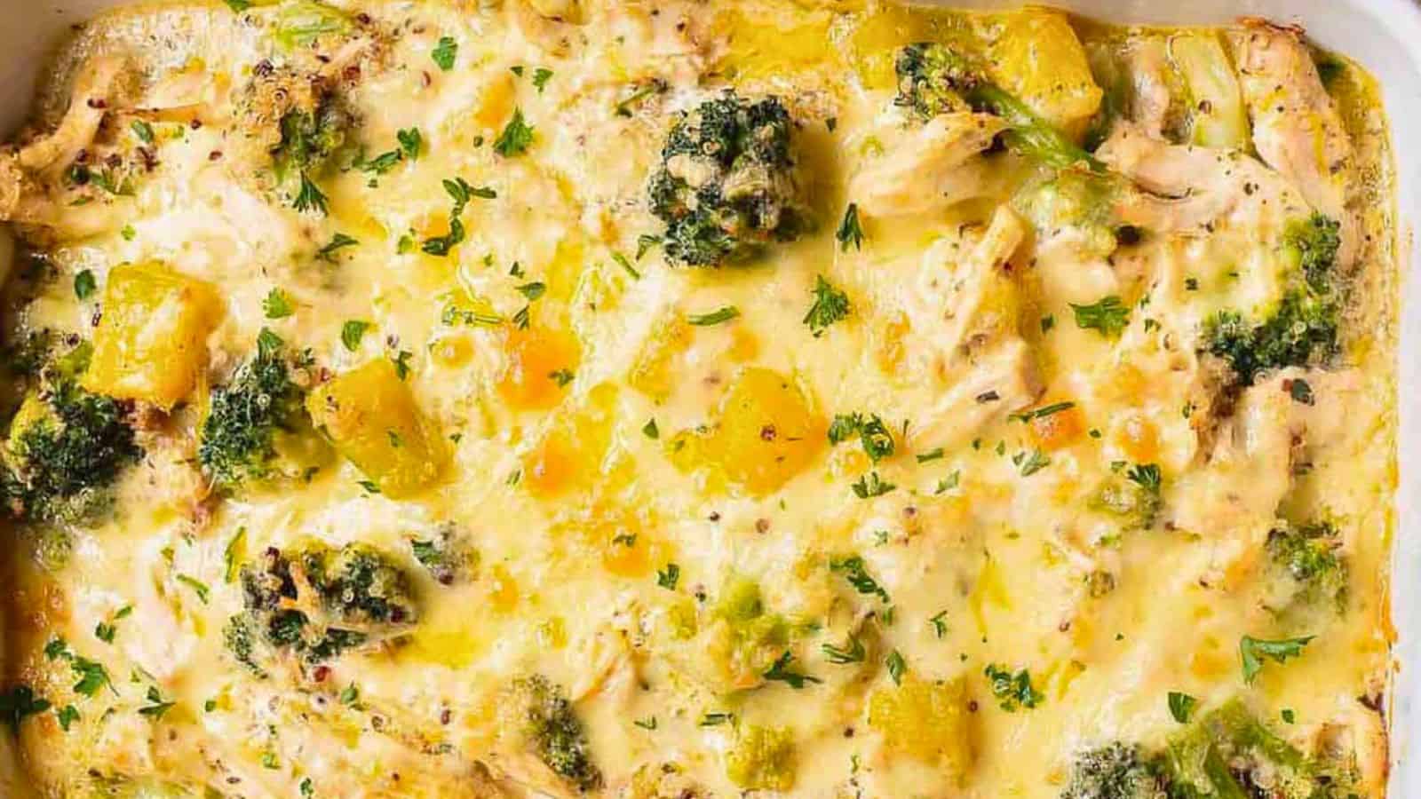 A baked casserole dish containing a cheesy broccoli and chicken mixture, topped with pieces of pineapple and sprinkled with chopped parsley.