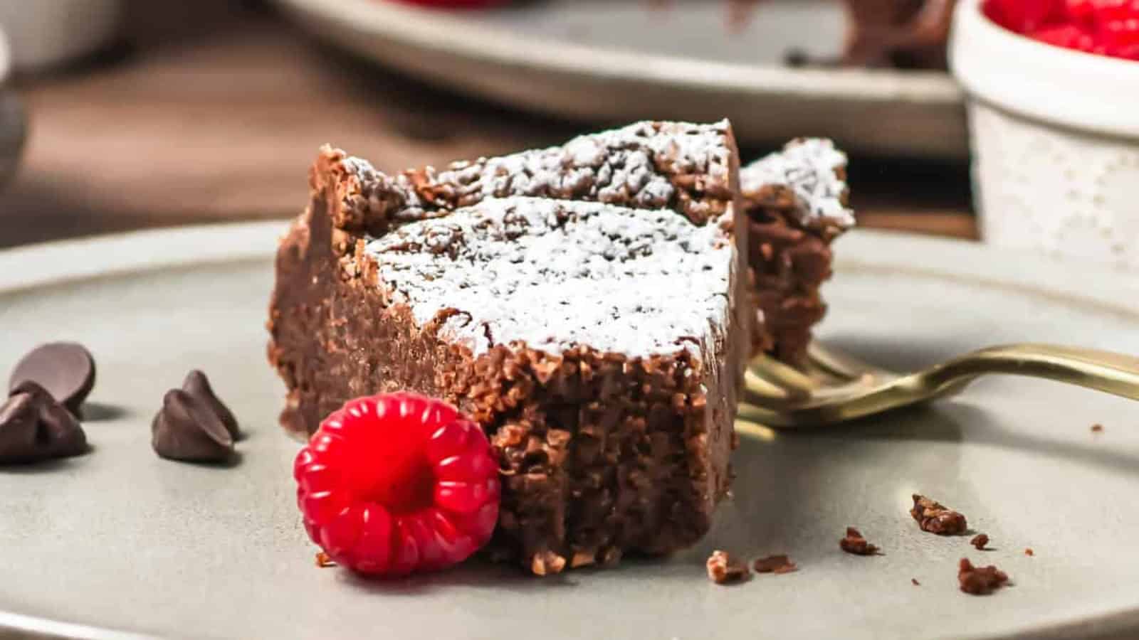 A chocolate cake dusted with powdered sugar, with raspberries and a cup of coffee on a wooden table.