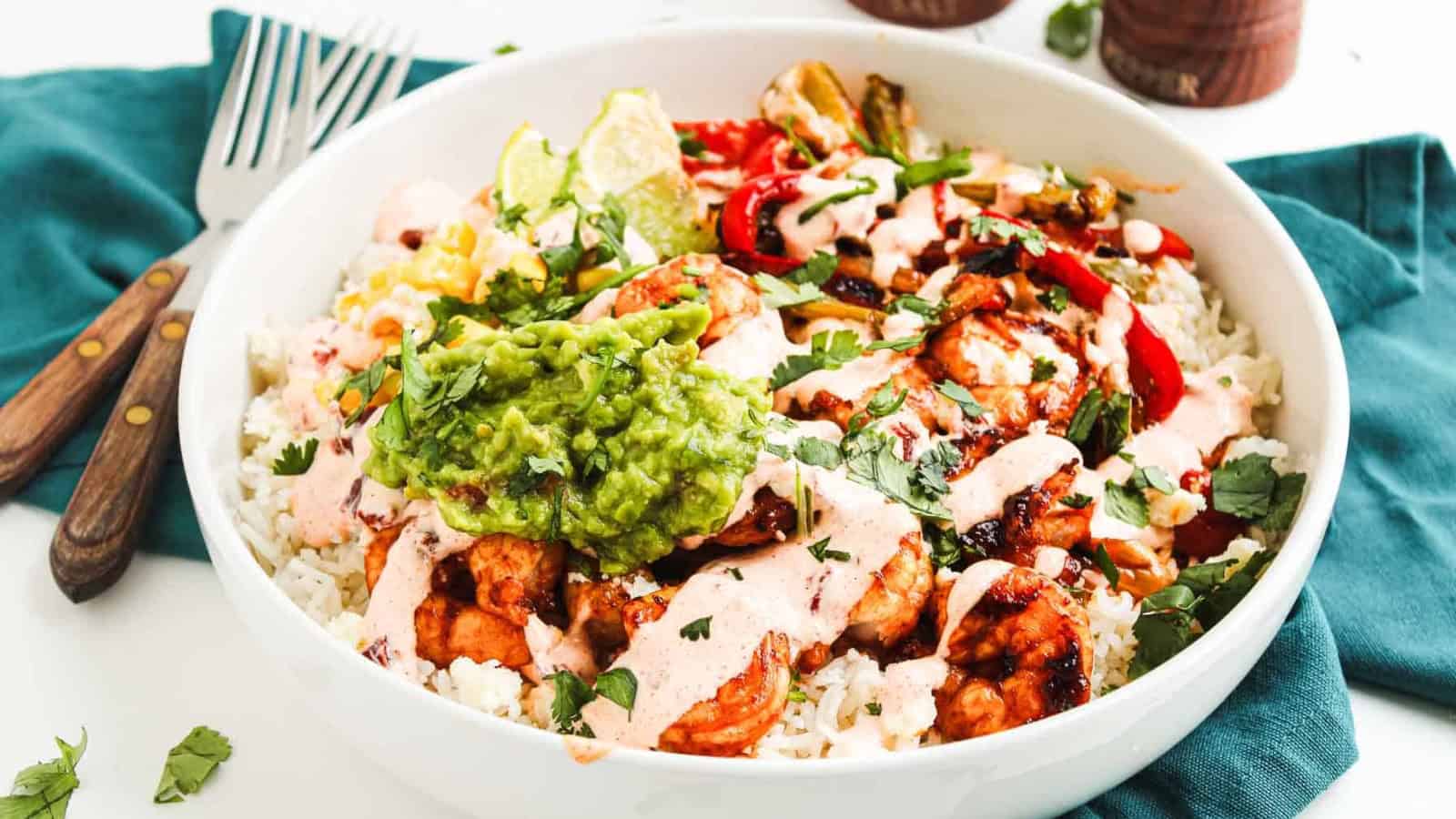A burrito bowl with rice, grilled chicken, guacamole, veggies, sauce, and cilantro in a white bowl.