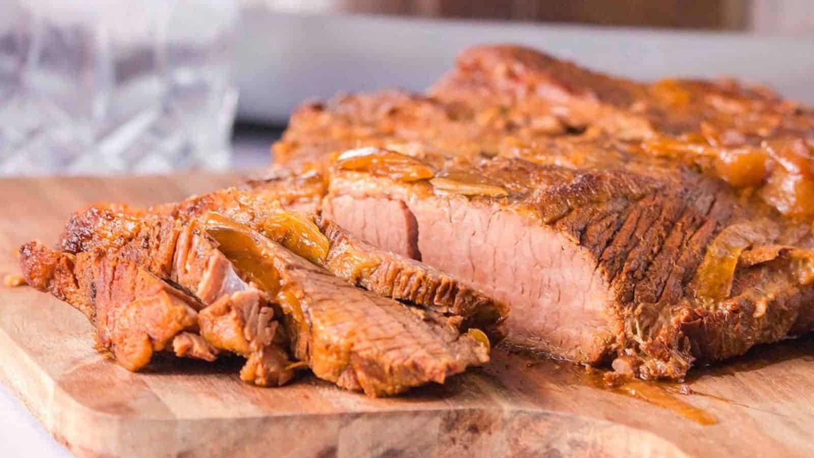 Sliced cooked brisket on a wooden cutting board with visible juices and onions.