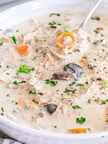 Creamy chicken and wild rice soup with carrots and mushrooms in a white bowl, served with bread.