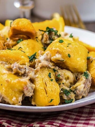 A plate of creamy gnocchi with herbs and golden roasted potatoes on a red checkered cloth.