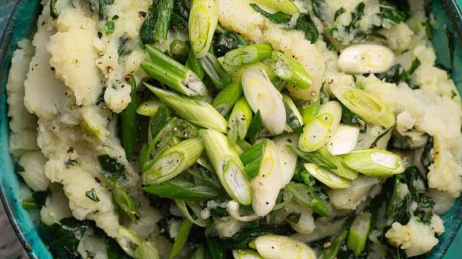 Mashed potatoes mixed with chopped green onions and leafy greens in a bowl.