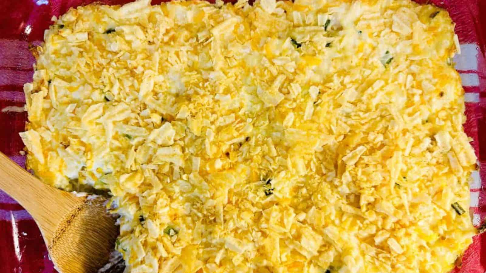 A casserole dish with shredded cheese and a wooden spoon.