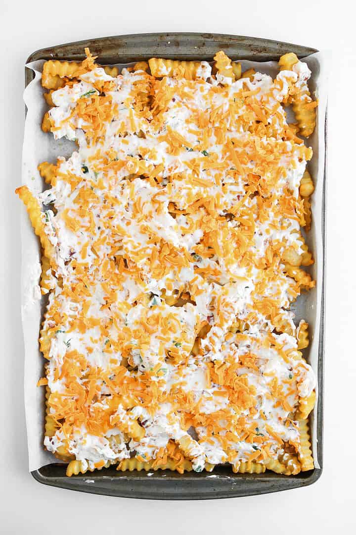 A sheet pan of crinkle-cut fries topped with melted cheese, creamy white sauce, and a kick of heat&mdash;your new favorite jalapeno popper loaded cheese fries recipe.