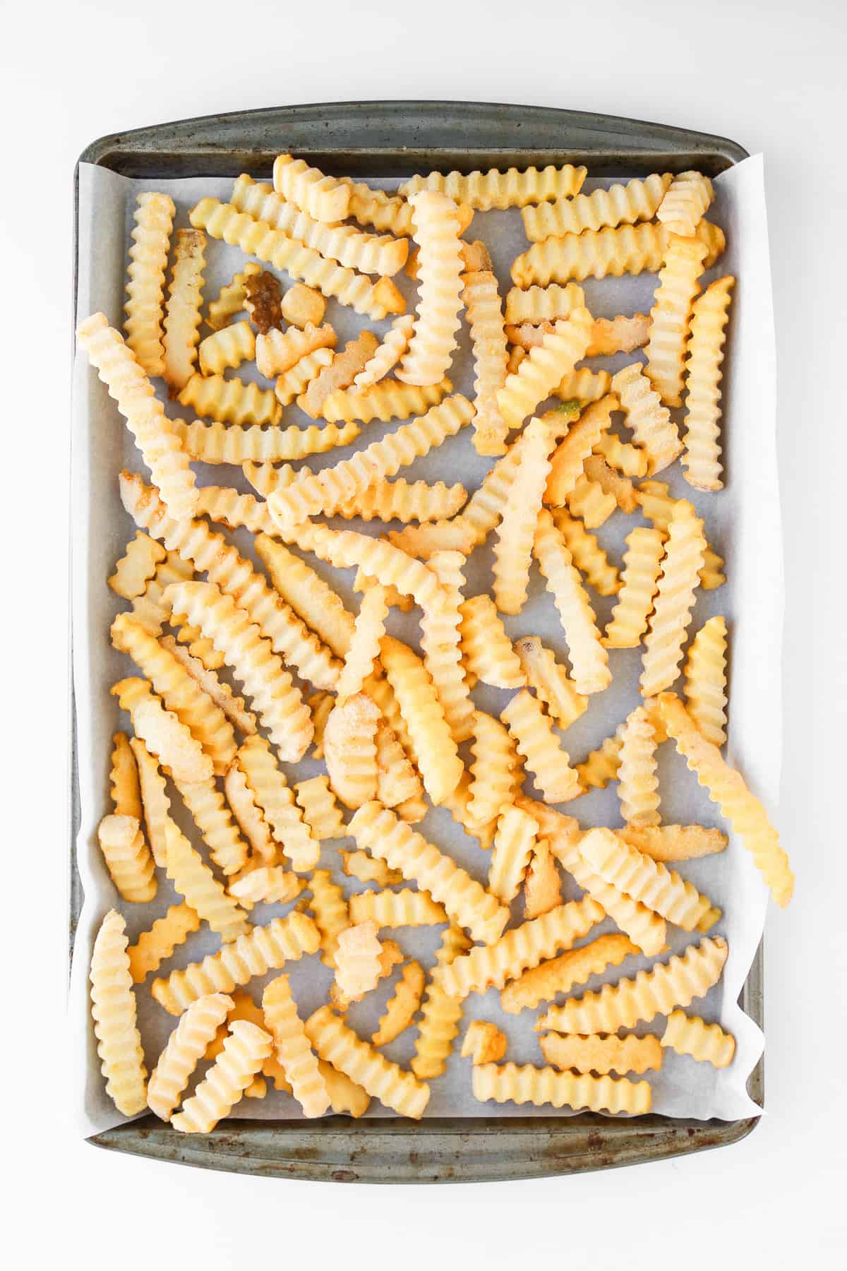 Crinkle-cut French fries spread on a baking sheet lined with parchment paper, ready for the ultimate jalapeno popper loaded cheese fries recipe.