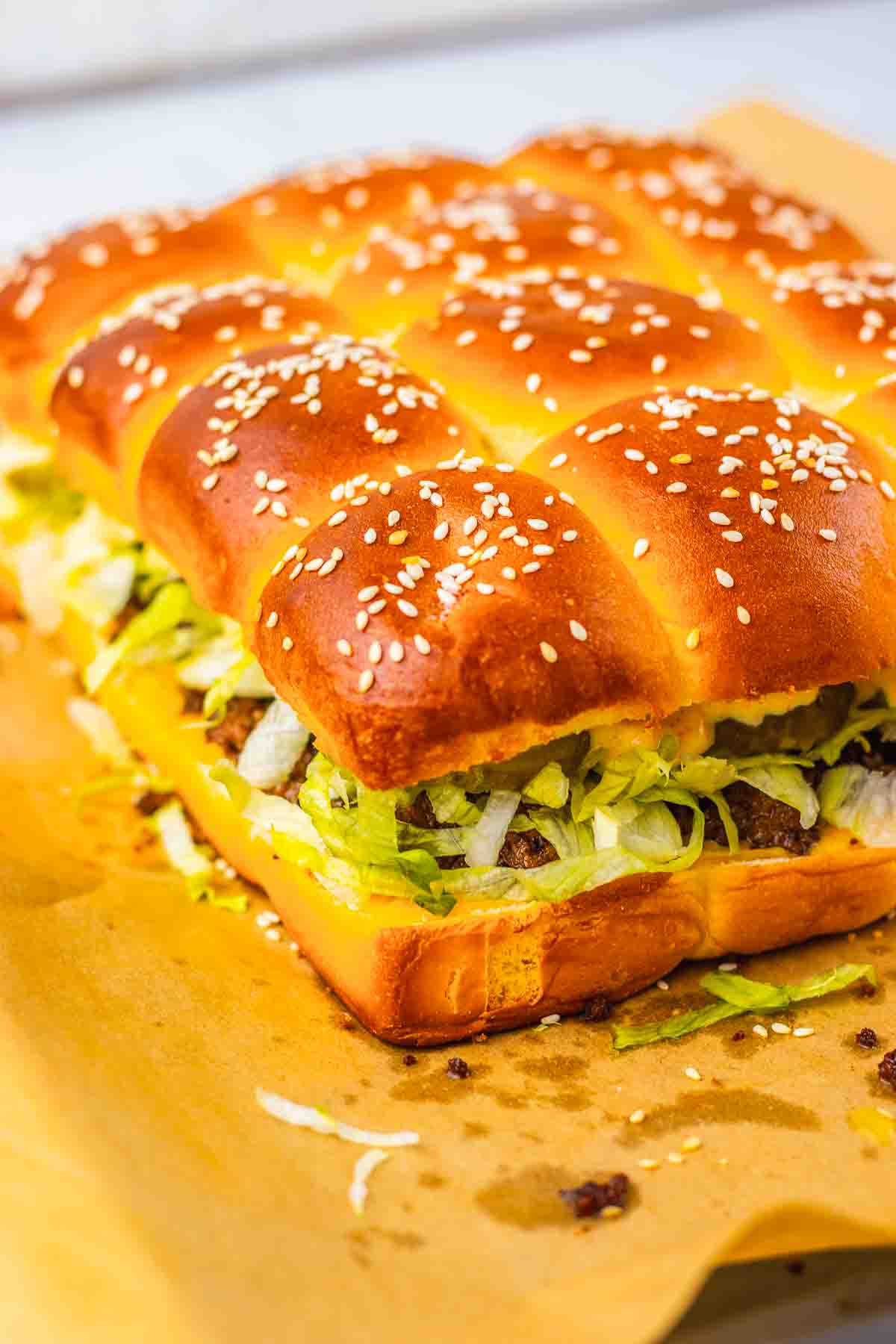 A pull-apart sandwich with sesame buns, lettuce, cheese, and beef on parchment paper&mdash;these homemade Big Mac Sliders are perfect for sharing.