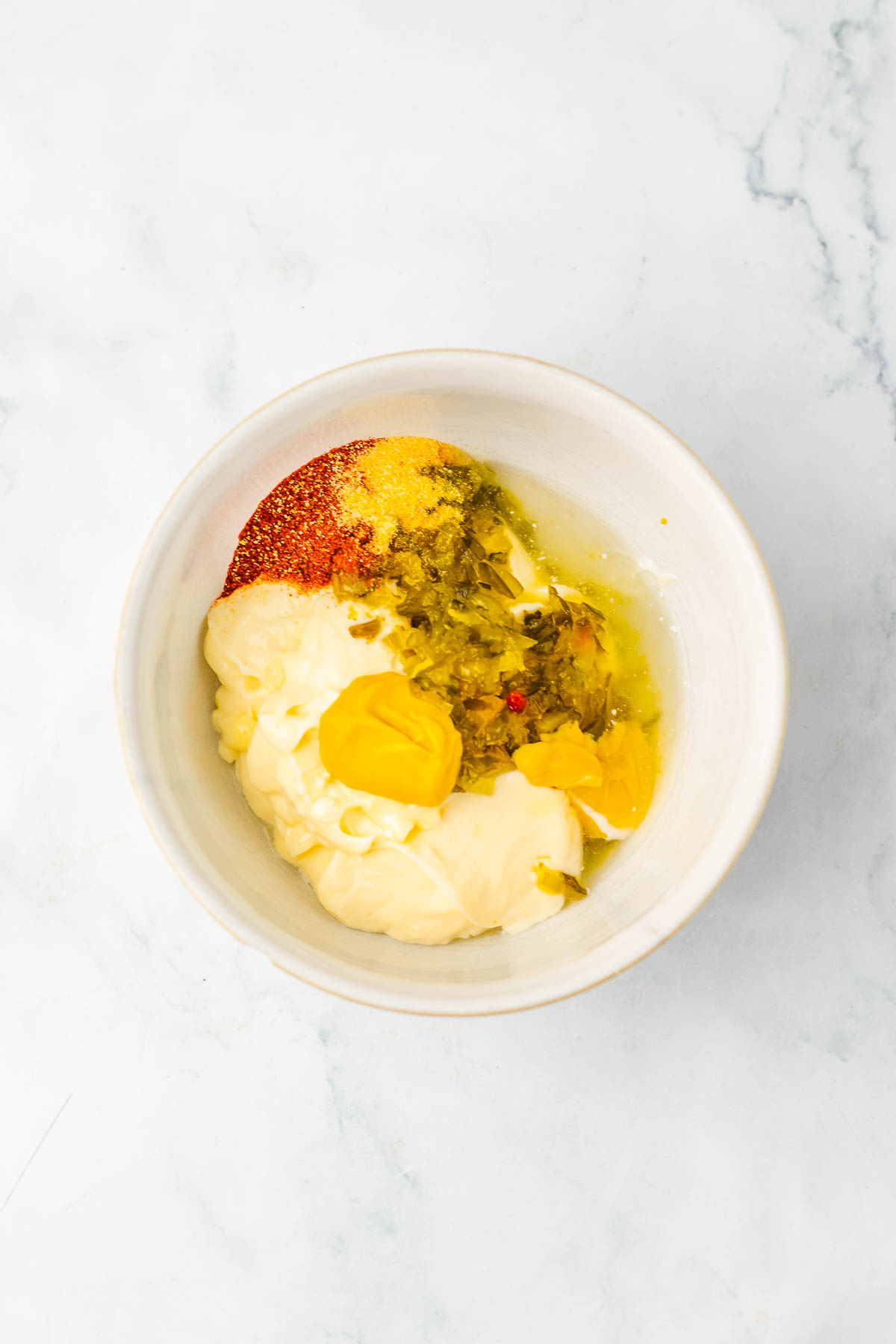 A white bowl with mayonnaise, mustard, relish, spices, and an egg yolk on a marble surface&mdash;perfect for making the classic sauce for Big Mac Sliders.