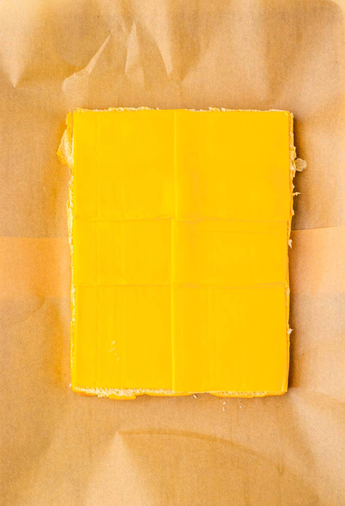 A square of sandwich bread topped with four slices of yellow processed cheese on brown parchment paper, perfect for assembling Big Mac Sliders or your favorite homemade sliders.