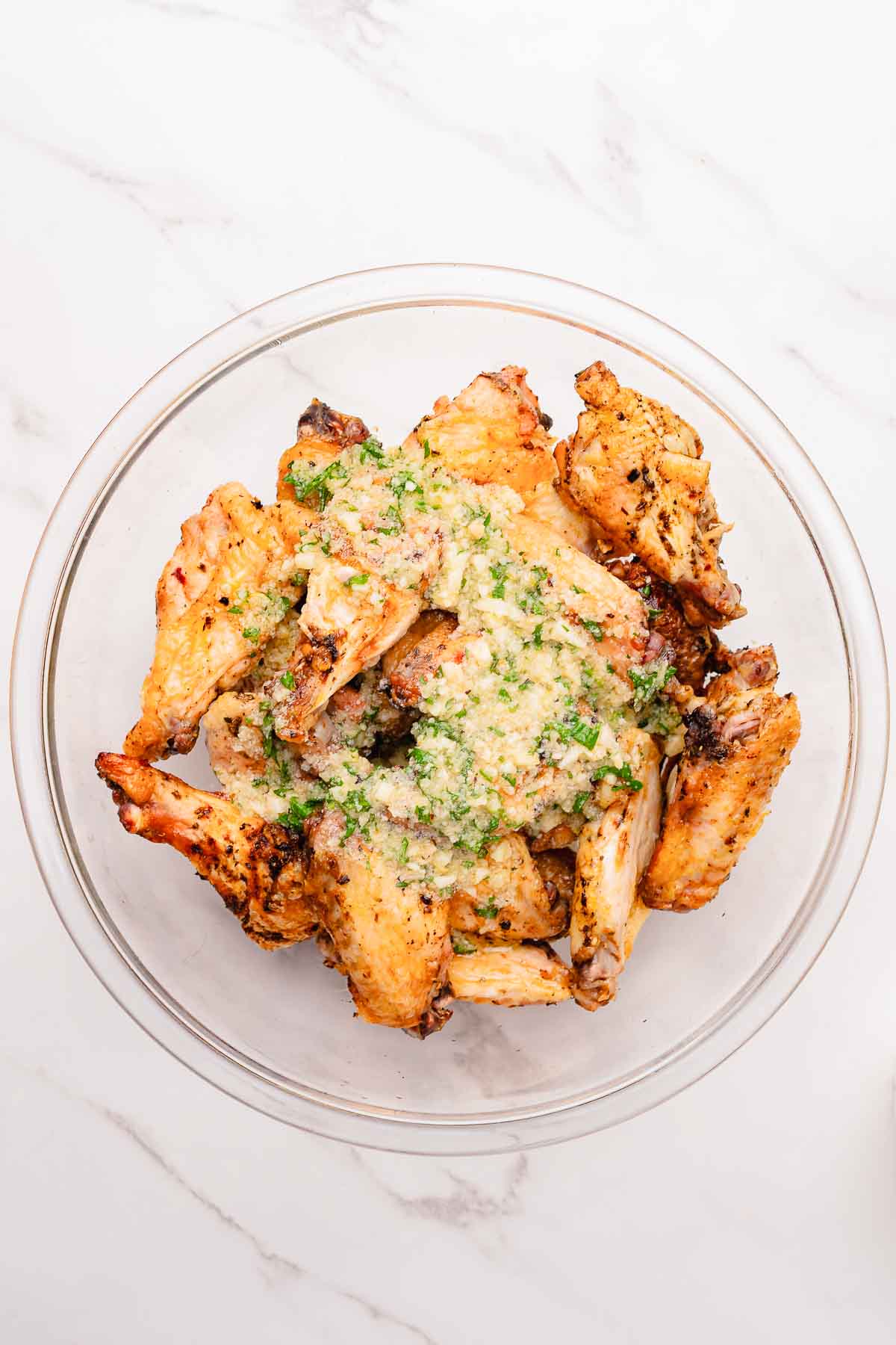 A bowl of crispy Chicken Wings topped with creamy Garlic Parmesan sauce sits on a white marble surface, fresh from the Air Fryer.