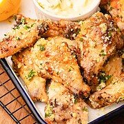 Crispy Garlic Parmesan chicken wings topped with herbs and cheese, served with lemon halves and a bowl of dipping sauce.