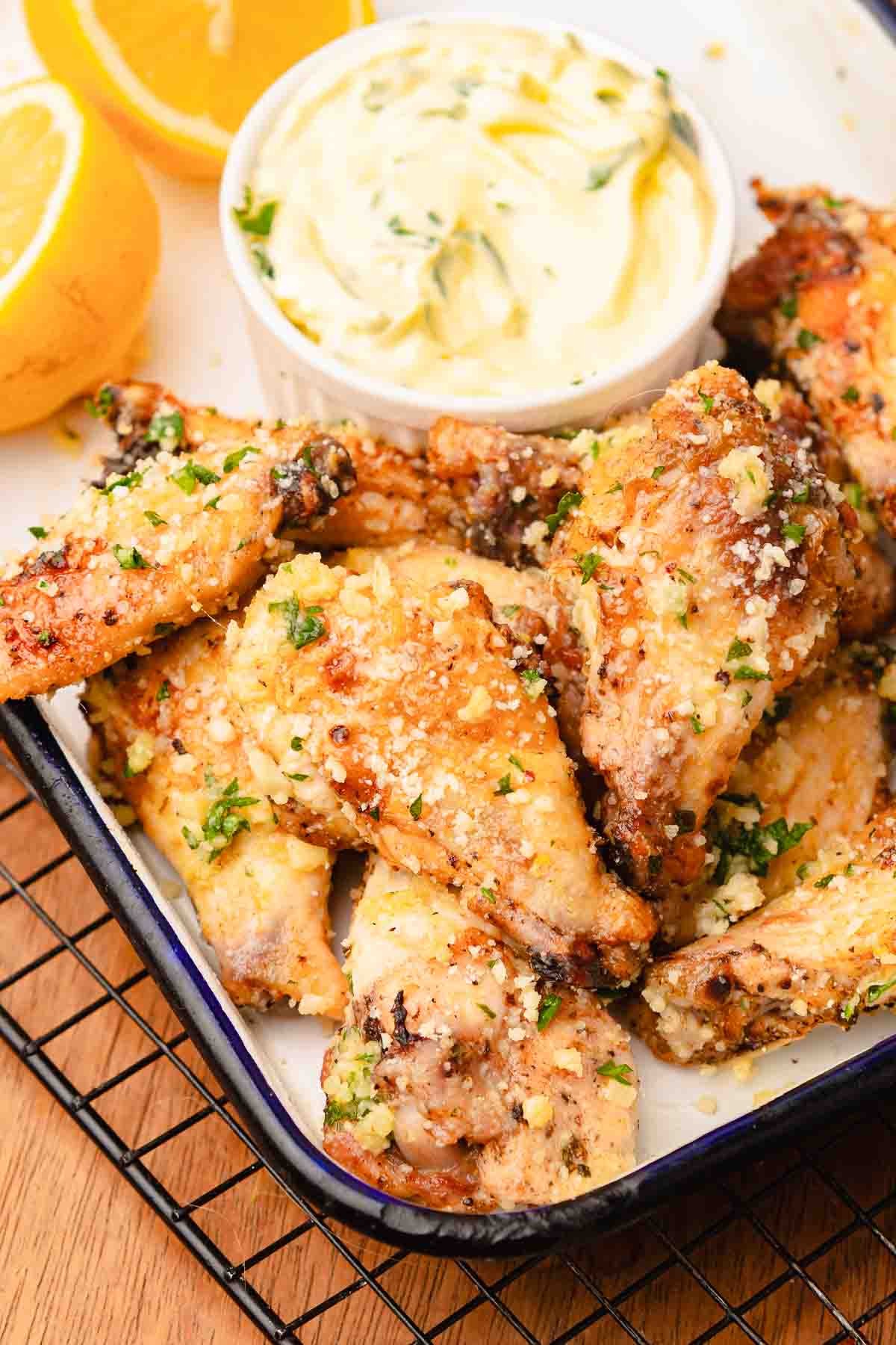 Crispy Garlic Parmesan chicken wings topped with herbs and cheese, served with lemon halves and a bowl of dipping sauce.