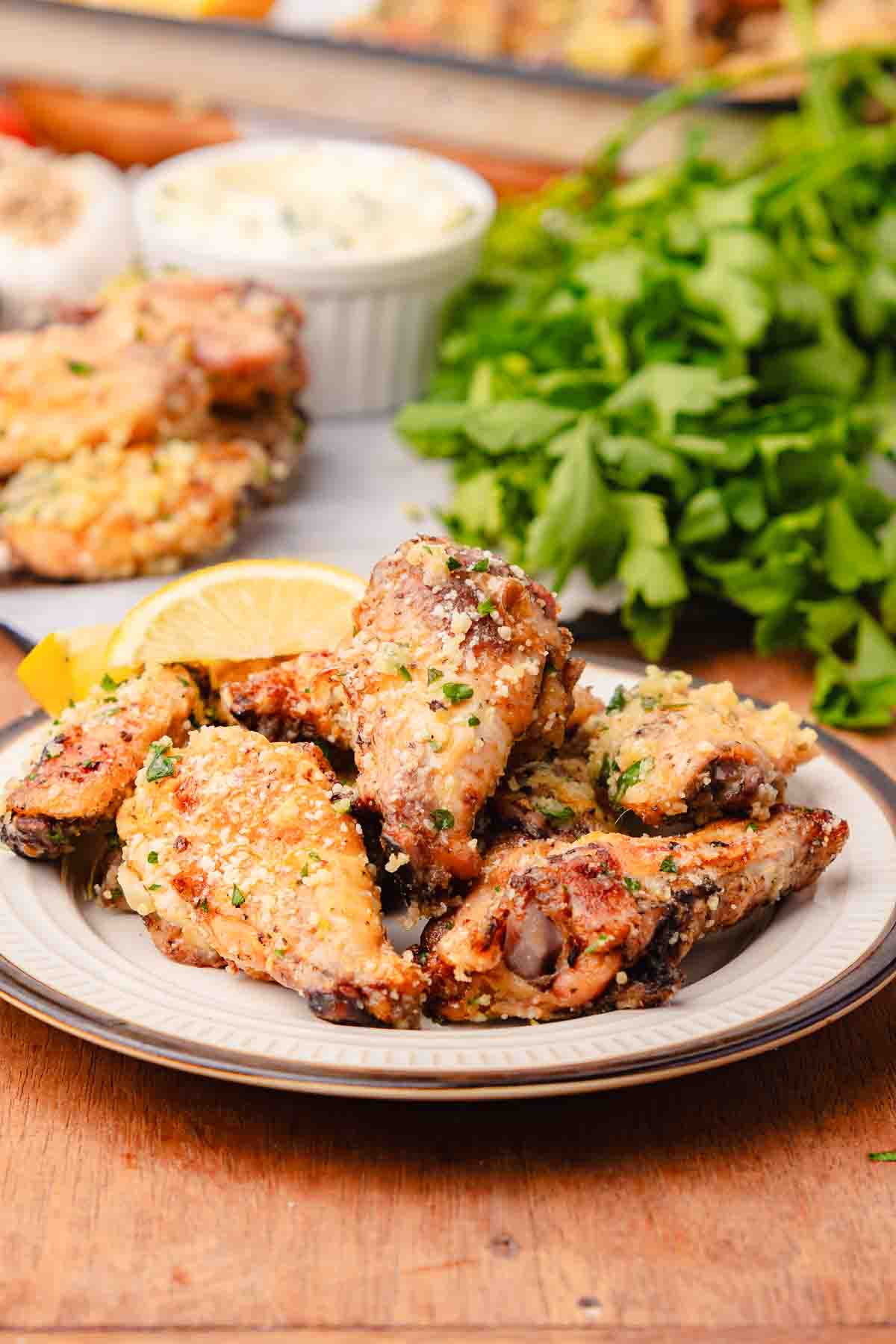 A plate of crispy garlic parmesan chicken wings, cooked to perfection in an air fryer, served with lemon wedges and a parsley garnish on a wooden table.