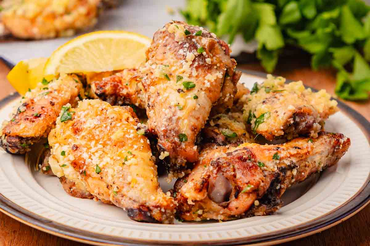 A plate of Garlic Parmesan Chicken Wings, cooked to perfection in an air fryer, garnished with herbs, grated cheese, and a slice of lemon.
