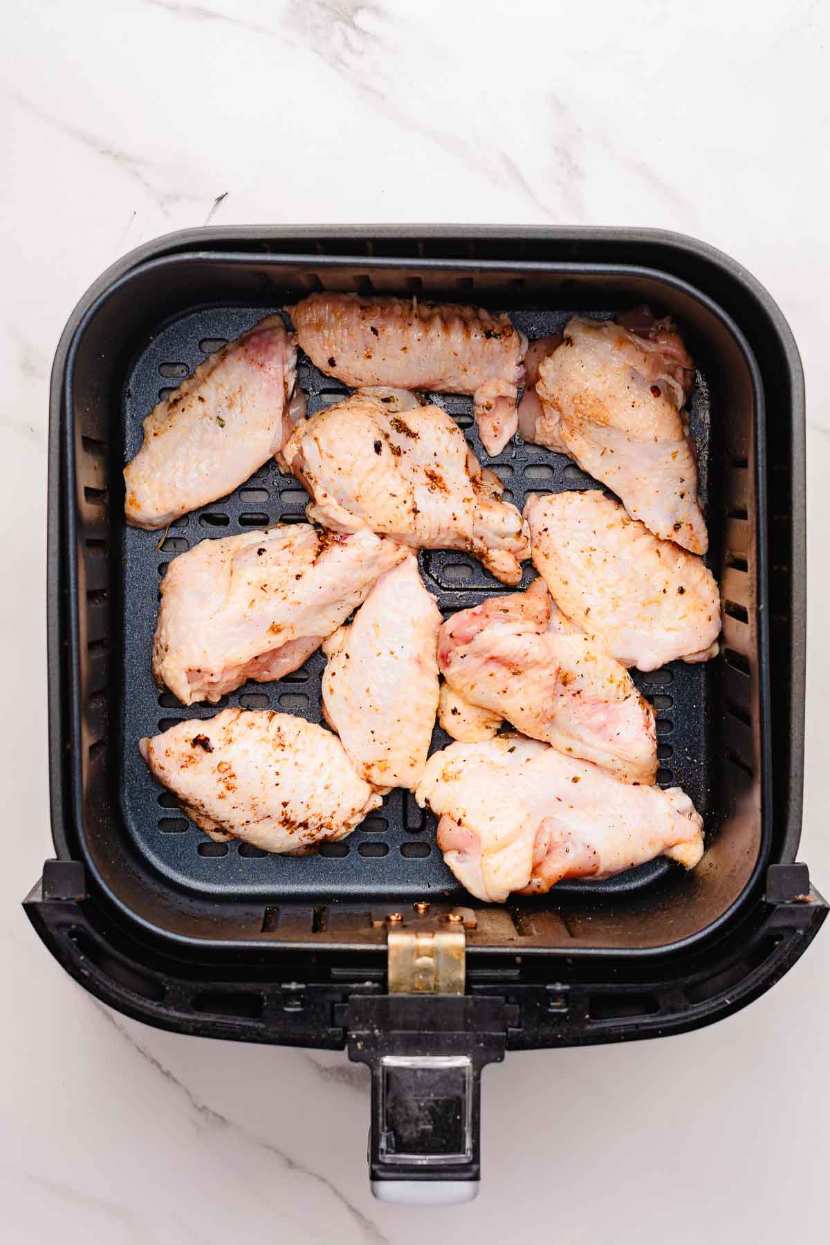Raw garlic parmesan chicken wings arranged in a single layer inside an air fryer basket on a marble surface.