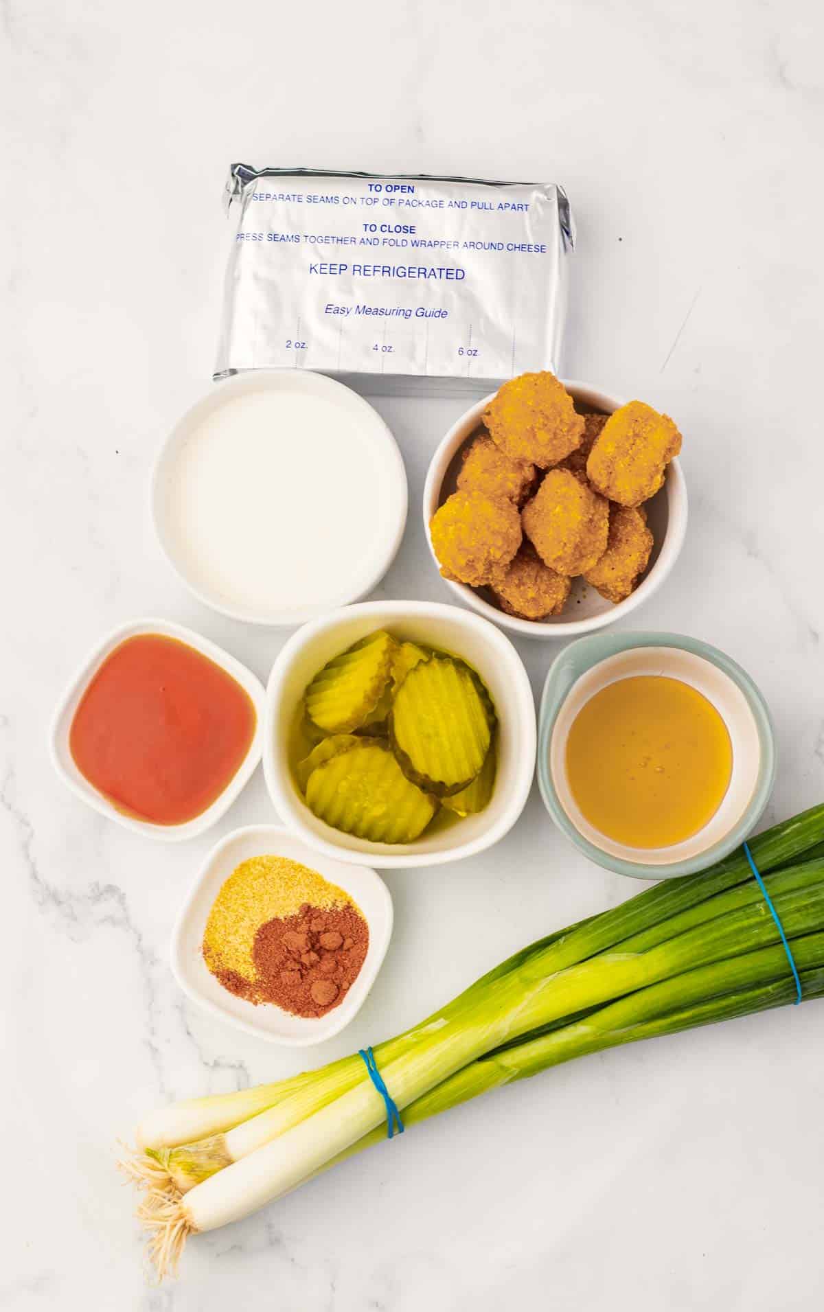 Ingredients for a delicious Hot Chicken Recipe laid out, including nuggets, pickles, sauces, cornstarch, spices, and green onions.