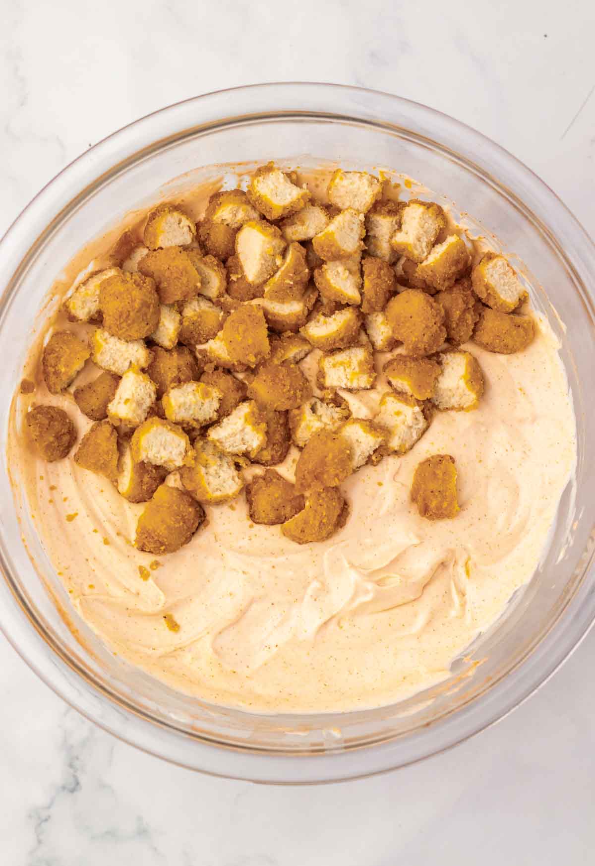 A glass bowl of creamy pumpkin mixture topped with chunks of golden cookie pieces on a marble surface&mdash;an irresistible fall recipe to try.