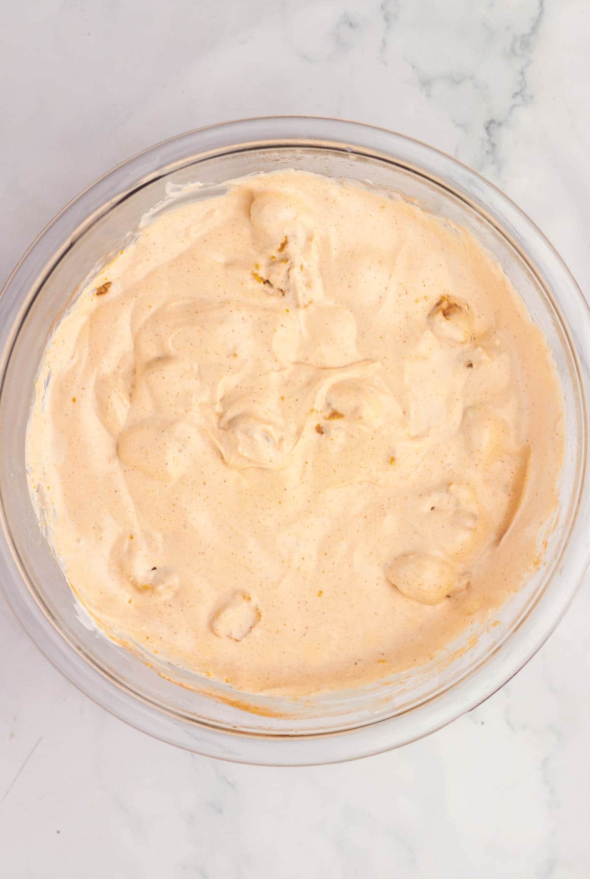A glass bowl filled with creamy, light orange Nashville Hot Chicken dip sits on a marble surface.