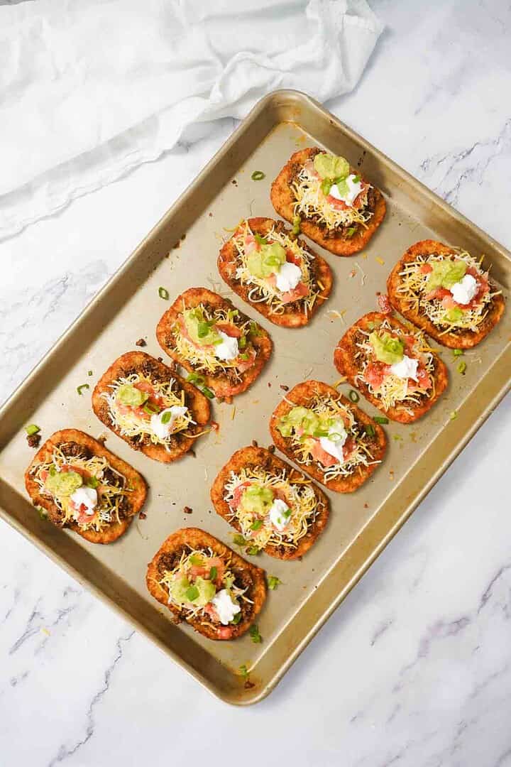 A baking tray with ten mini Mexican pizzas topped with cheese, sour cream, guacamole, and a delicious beef taco filling on a marble surface—perfect for trying a new recipe.