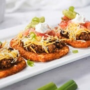 Three loaded Beef Taco bites with ground beef, shredded cheese, salsa, sour cream, and green onions on a white tray—an irresistible recipe perfect for any occasion.