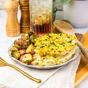 A plate of mashed potatoes with Parmesan Chicken, roasted potatoes, and broccoli, next to a glass of iced drink.