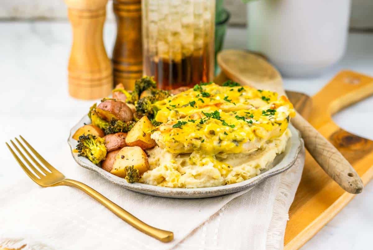 Plate of mashed potatoes, roasted broccoli and potatoes, and creamy chicken, served with a fork on a napkin for an easy sheet pan dinner.