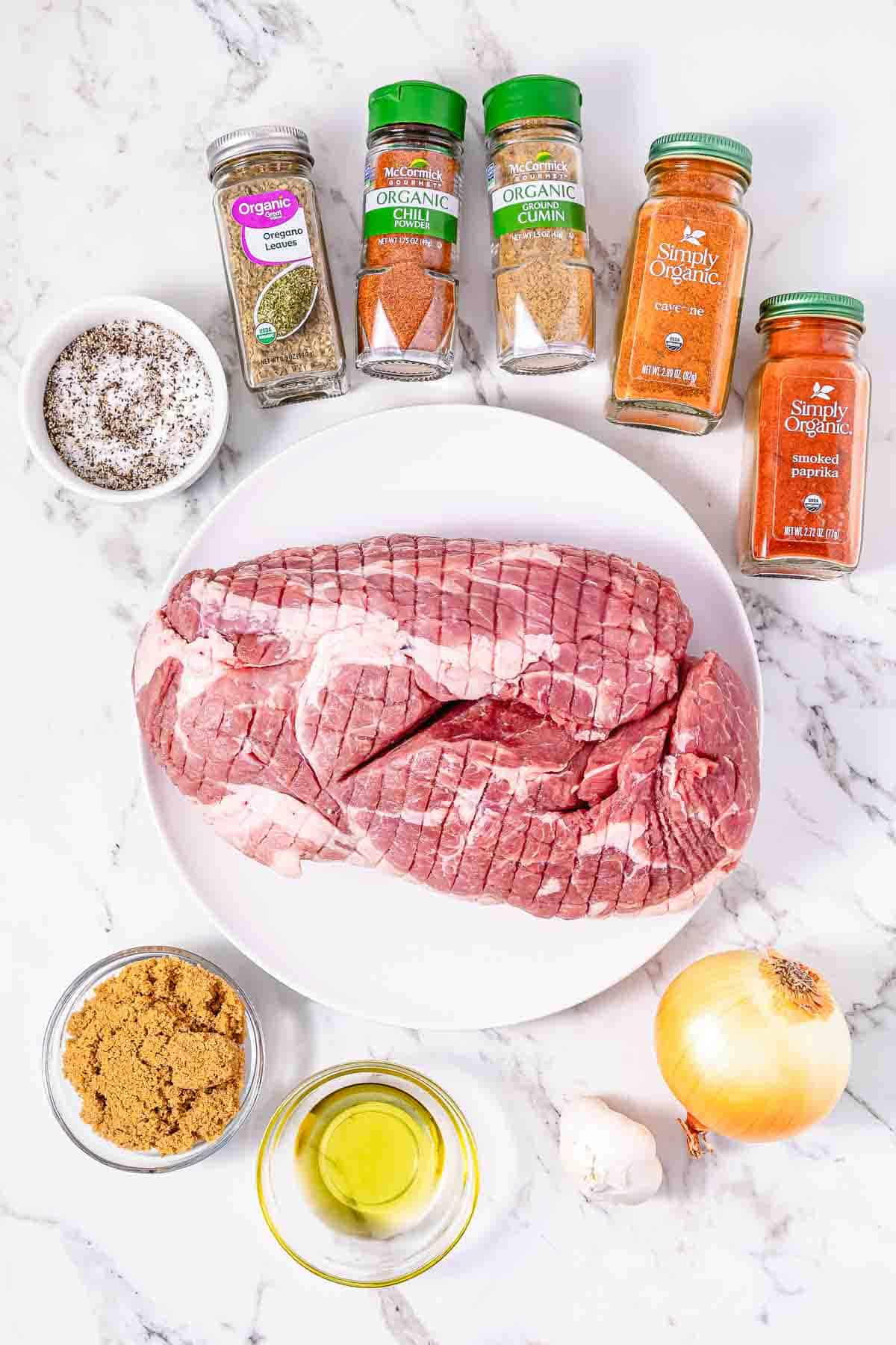 Raw pork roast on a plate with spices, brown sugar, olive oil, onion, and garlic on a marble surface—perfect for a savory Crockpot BBQ Pulled Pork sandwich recipe.