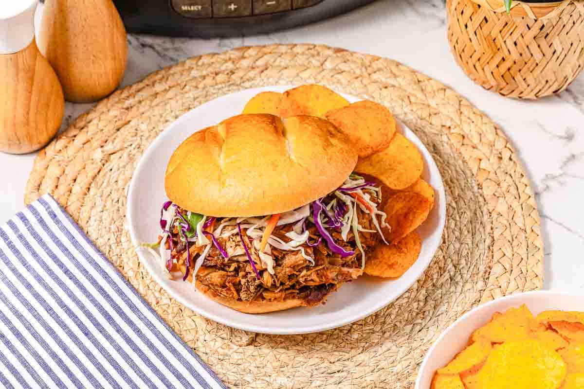 BBQ Pulled Pork sandwich with coleslaw and chips on a white plate, set on a woven placemat—an irresistible sandwich recipe perfect for any meal.