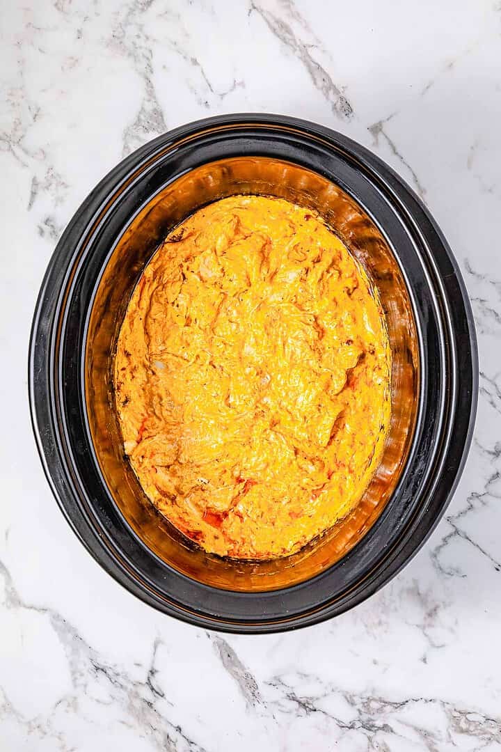 A Crockpot filled with creamy, orange-colored Buffalo Chicken Dip sits on a marble countertop.