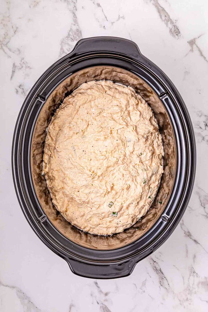 A Crockpot filled with uncooked cheesy Crab Dip mixture sits on a marble countertop, ready for your next recipe adventure.