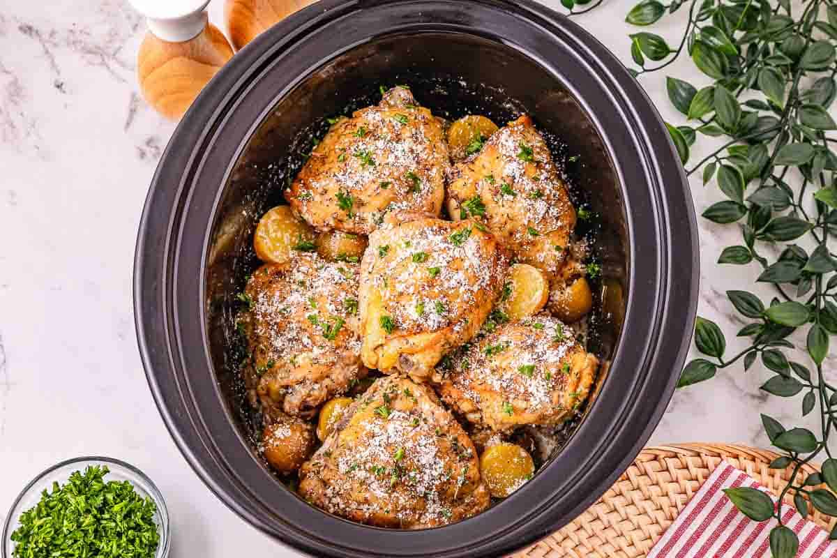 Slow cooker chicken thighs with baby potatoes and herbs, topped with grated cheese and parsley&mdash;a comforting Crockpot chicken dinner.