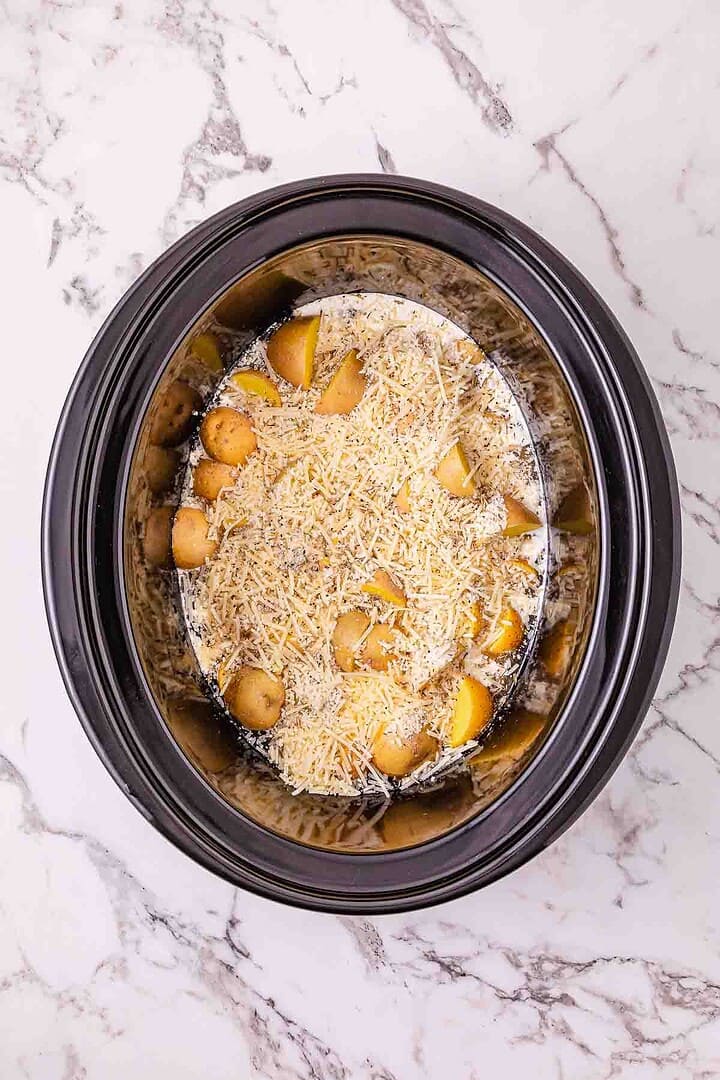Slow cooker chicken with baby potatoes topped with shredded cheese, seen from above on a marble surface&mdash;perfect for an easy Crockpot chicken dinner.