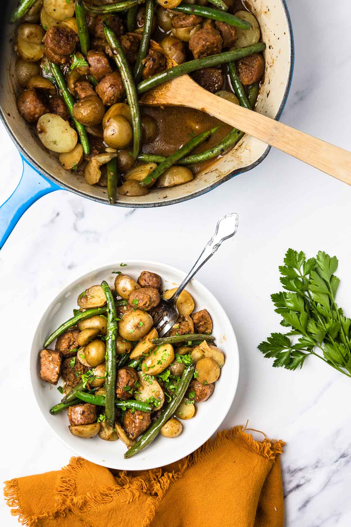 A bowl of sausage, potatoes, and green beans sits next to a pan of the same dish&mdash;perfect for those who love comfort food. Try a Vegetarian Swamp Potatoes version for a meat-free twist, with fresh parsley and a fork nearby.