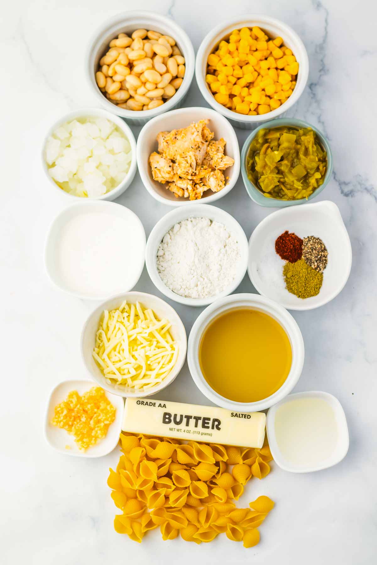 Twelve bowls with pasta, butter, cheese, corn, milk, beans, spices, onion, flour, broth, and diced ingredients&mdash;perfect for whipping up a hearty Chicken Chili Mac or classic White Chicken Chili.
