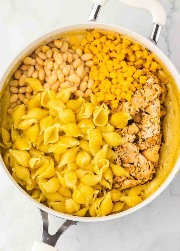 A pot with cooked shell pasta, white beans, corn, and crumbled seasoned tofu, reminiscent of a comforting Chicken Chili Mac, before mixing.