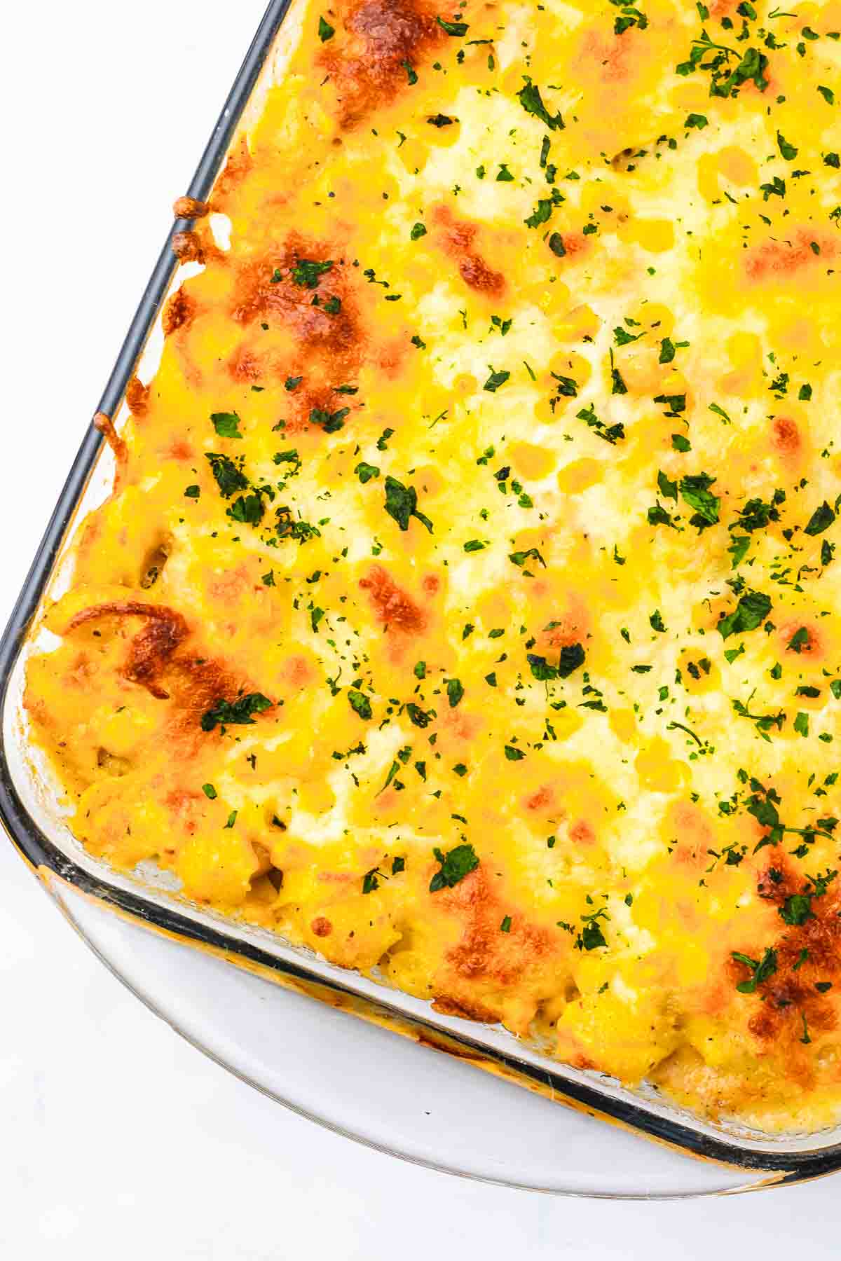 Golden baked Mac and Cheese casserole with melted cheese and parsley in a glass dish.