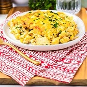 A plate of cheesy Mac and Cheese casserole with chicken and pasta, topped with herbs, sits next to a glass of ice water.