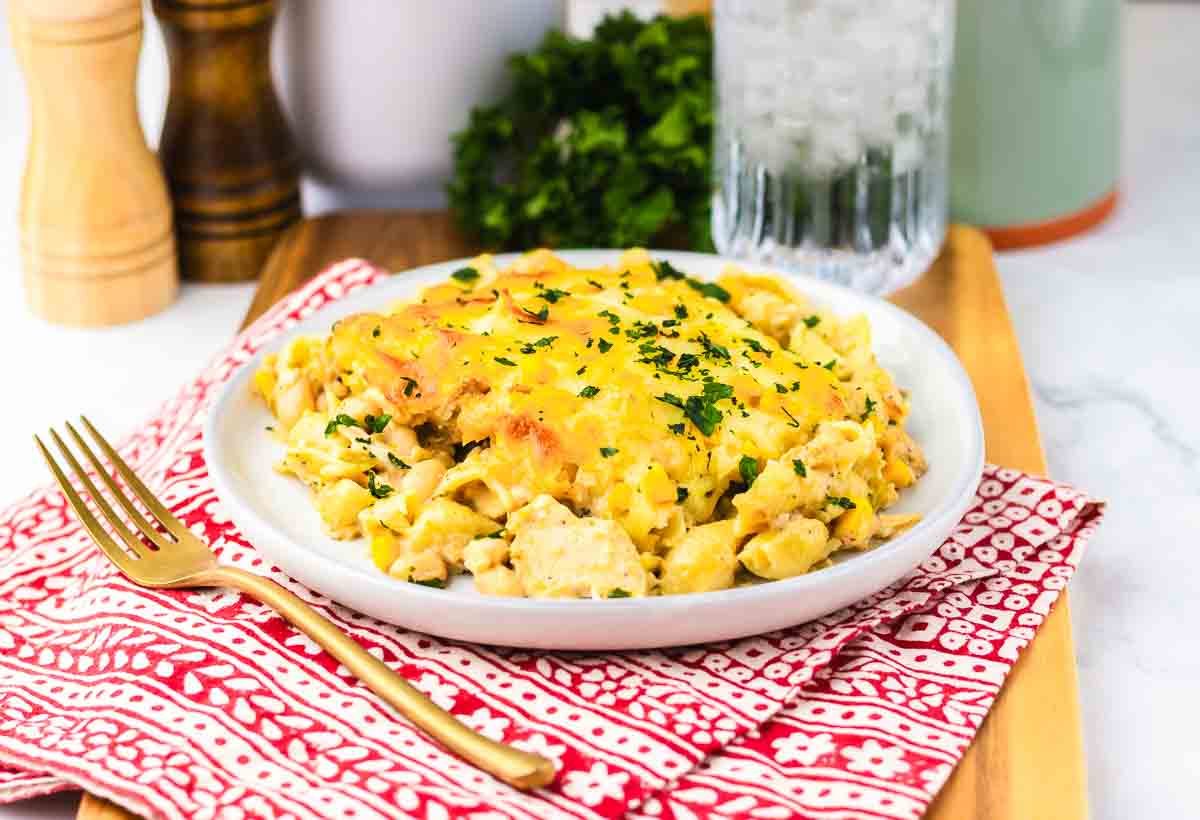 Plate of cheesy chicken casserole reminiscent of White Chicken Chili, topped with herbs on a red patterned napkin, with a gold fork beside it.
