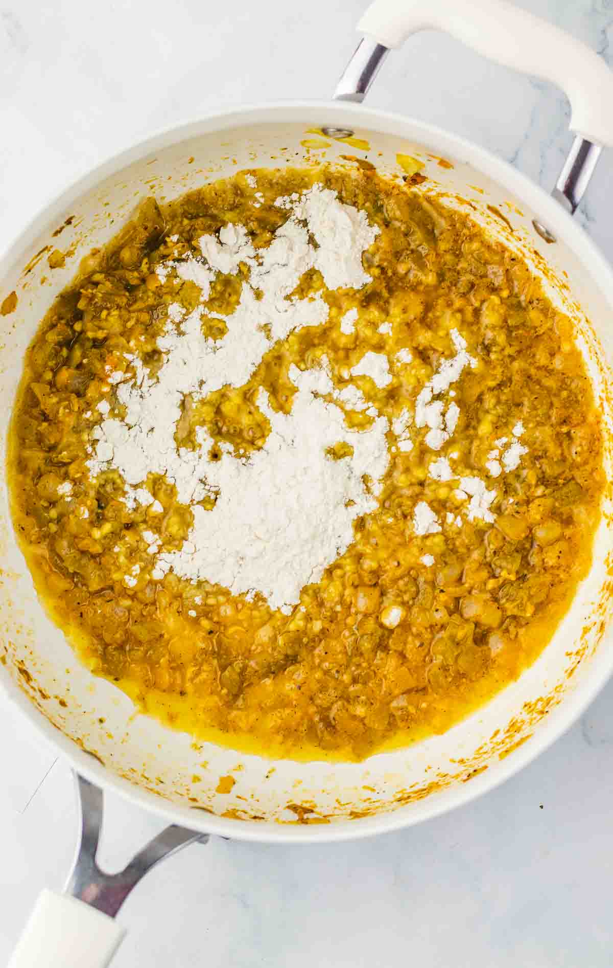 White flour sprinkled over a yellow lentil mixture cooking in a white pot on a marble surface, reminiscent of the creamy richness found in Mac and Cheese.